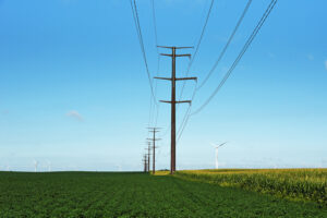 A photograph of power lines in a field with windmills in the background.